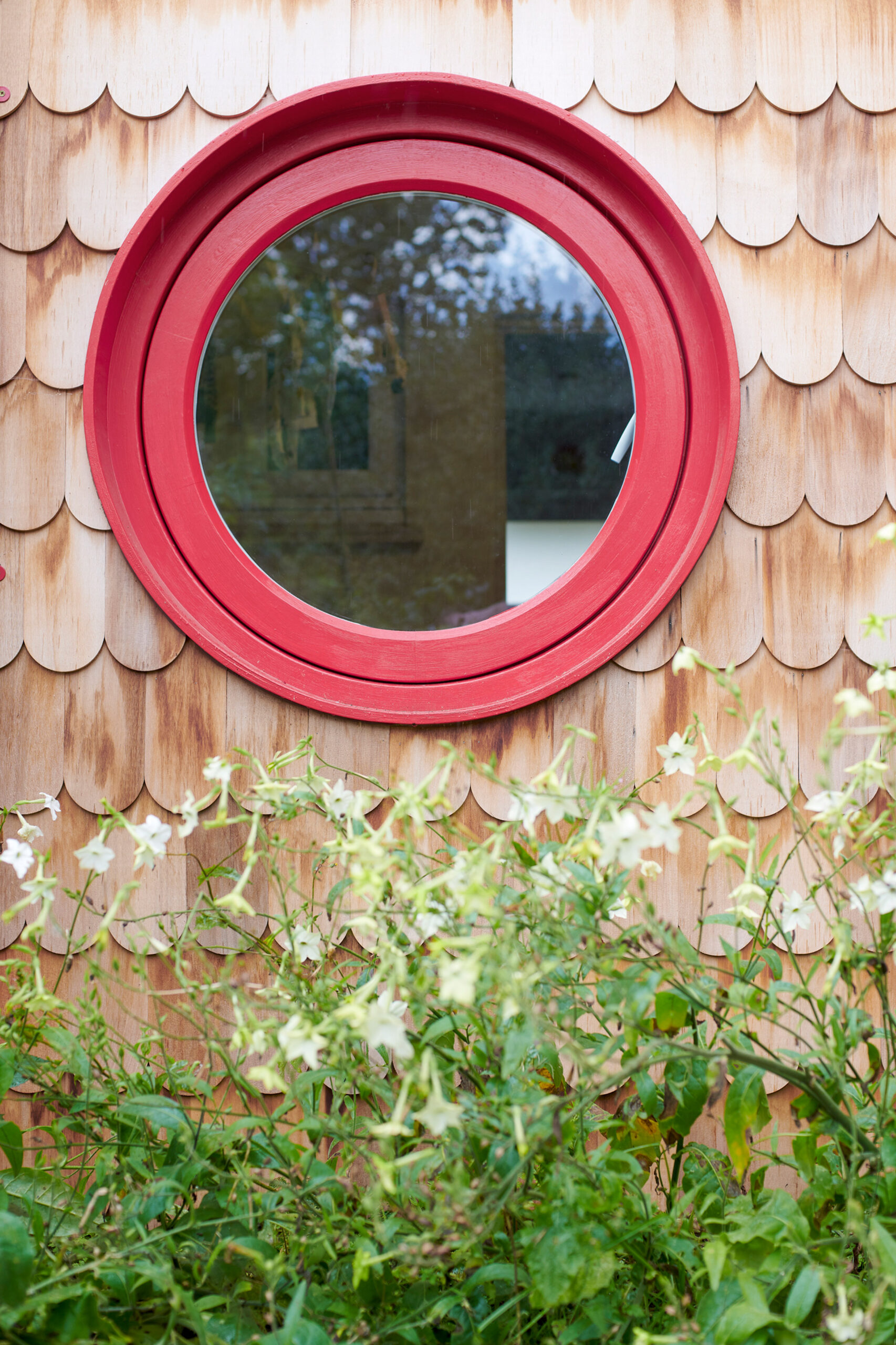 Round, red-framed window in a shingle wall